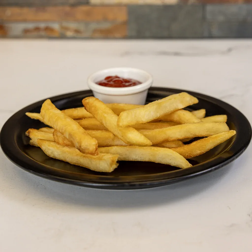 Golden French fries on a black plate with a small cup of ketchup.